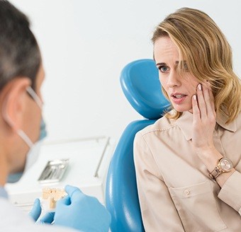 Woman in dental chair holding cheek